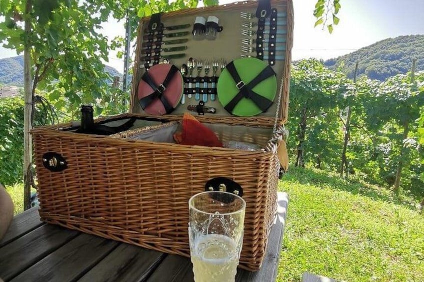 Una cesta de mimbre para picnic con una botella de vino, una copa y un sacacorchos sobre una mesa. 4