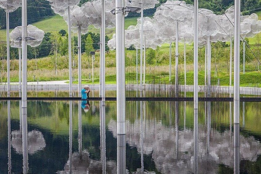 A person standing by a reflective water body with white structures overhead. 3