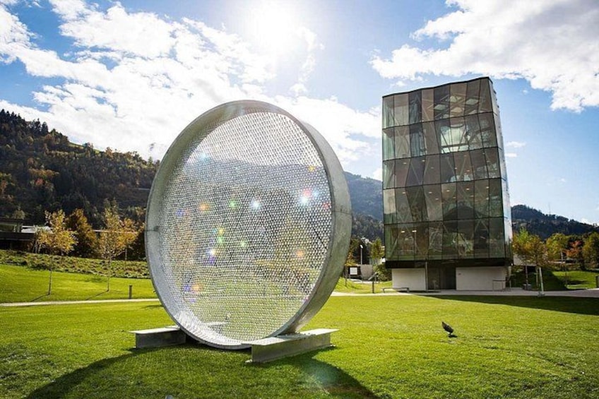 A large spherical structure with a reflective surface, a modern glass building, and a grassy field with a mountain in the background. 5