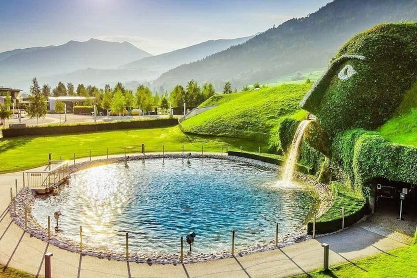 A circular pool with a waterfall feature, surrounded by a well-maintained lawn and a mountain backdrop. 1