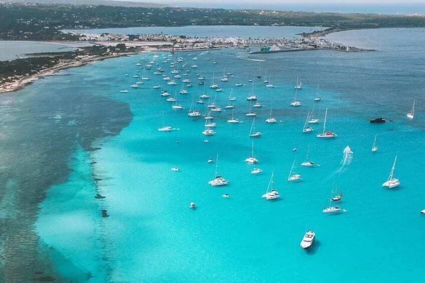 A coastal area with numerous sailboats anchored in turquoise waters. 1