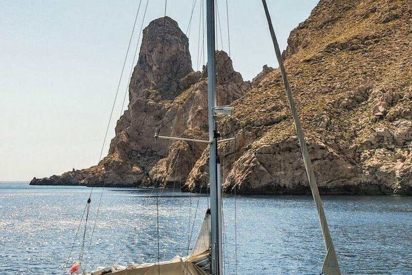 A sailboat with a mast and rigging, calm sea, rocky coastline, and a prominent rock formation. 4