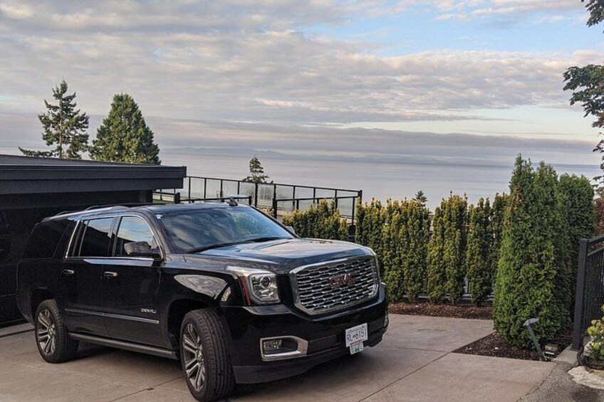 A black SUV parked on a driveway with a view of the ocean and trees in the background. 2