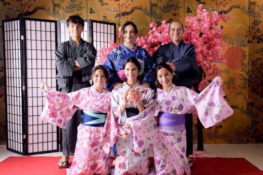 En familj klädd i traditionella japanska kimonos poserar framför en dekorativ bakgrund med körsbärsblommor. 1