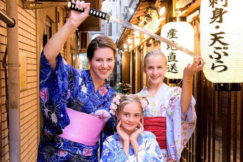 Een persoon in een blauwe kimono die een roze waaier vasthoudt, en een kind in een kimono met bloemen. 1