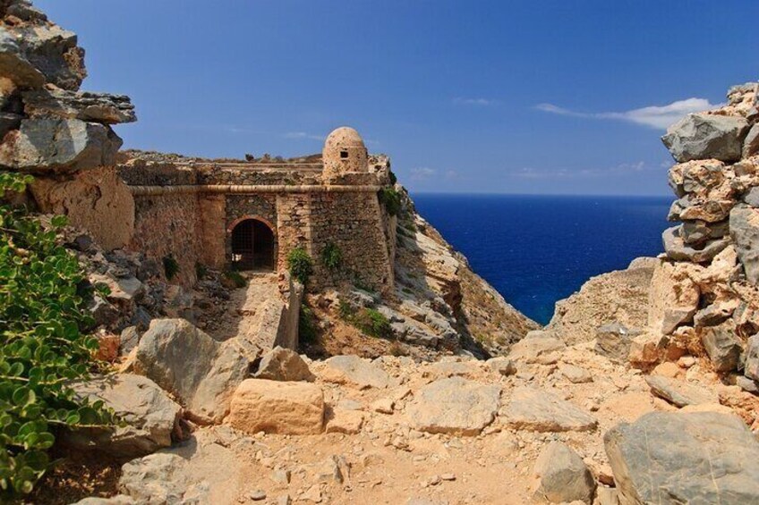A rocky coastal landscape with a historical stone building featuring a dome and arched entrance. 5