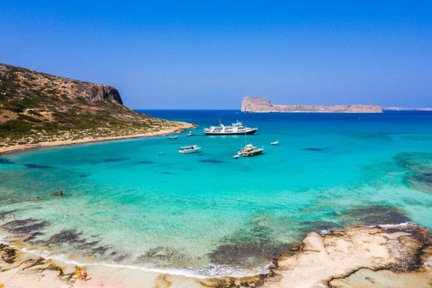 A coastal landscape with clear turquoise waters, boats, rocky shorelines, and distant cliffs. 3