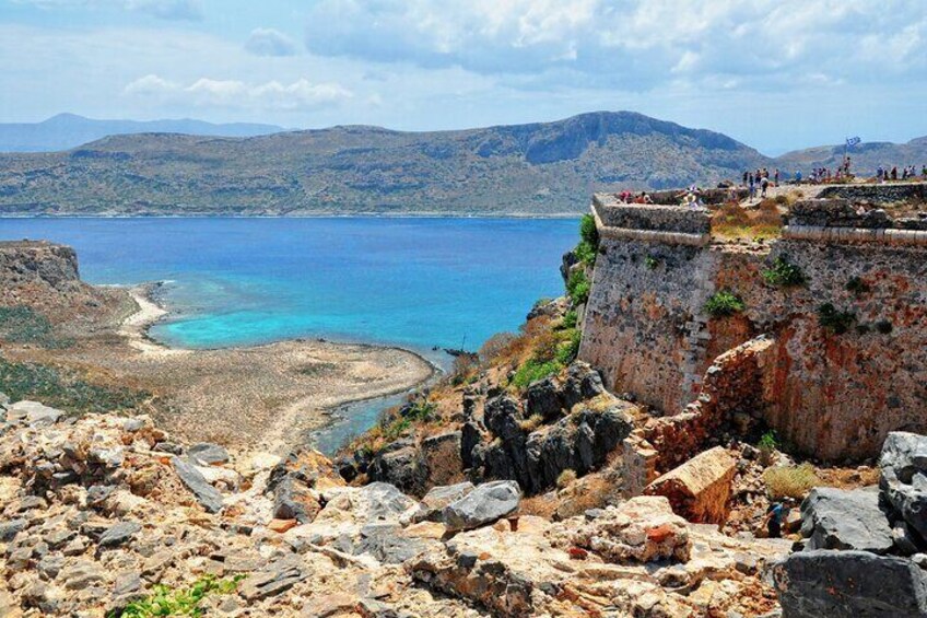A coastal landscape with a rocky cliff, a beach, and a clear blue sea. 4