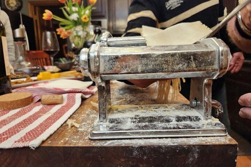 A vintage pasta machine on a wooden table with flour scattered around. 3