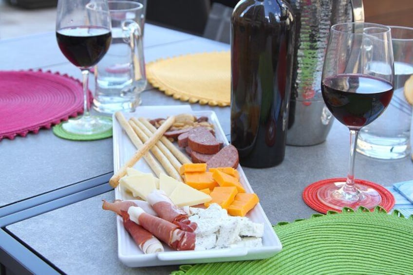 A charcuterie board with various cheeses, meats, and crackers on a table with wine glasses and a bottle. 2