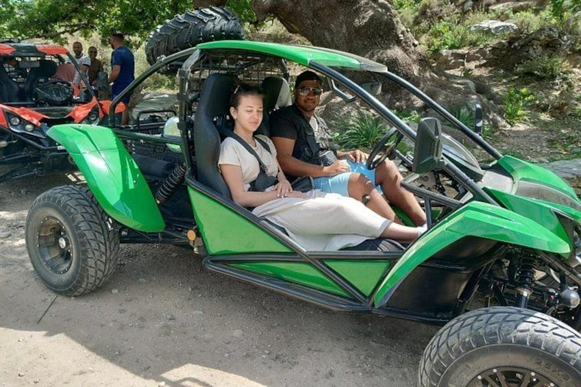 A green off-road vehicle with two people inside, parked on a dirt road. 3