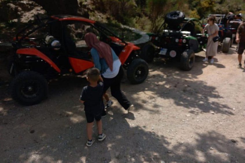 Un veicolo fuoristrada rosso e nero, una persona con un bambino e un altro veicolo in un ambiente naturale. 4