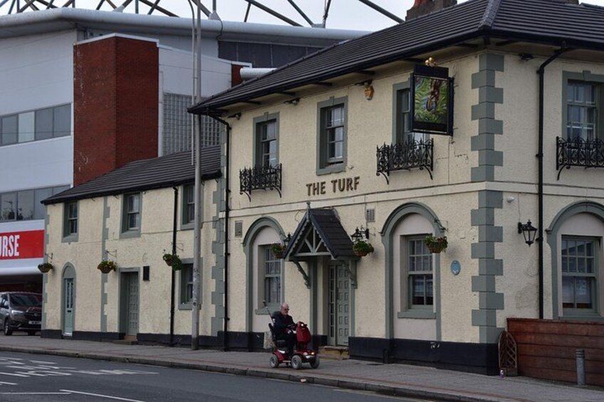 A building named 'The Turf' with a sign above the entrance, a street lamp, and a person riding a tricycle on the sidewalk. 2