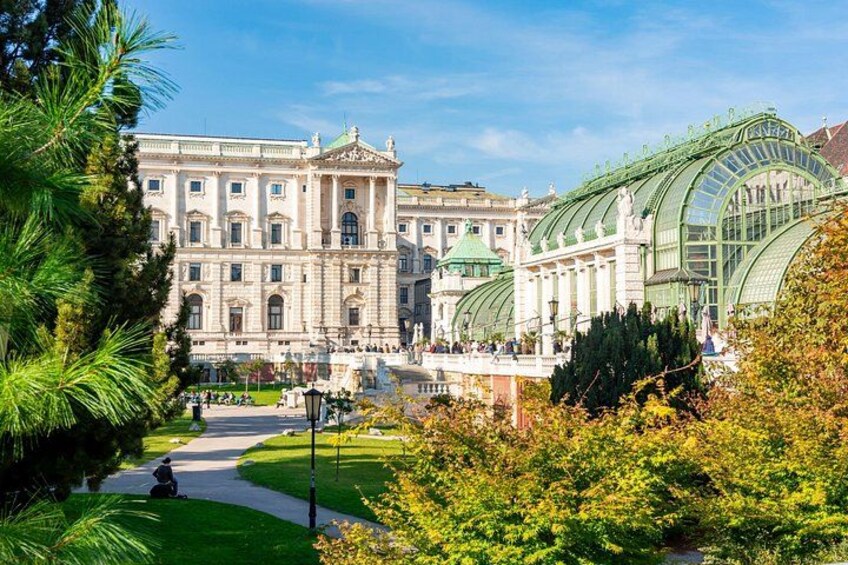 Ein prachtvolles Gebäude mit einem Wintergarten aus grünem Glas, umgeben von üppiger Vegetation und wolkenlosem, blauem Himmel. 4
