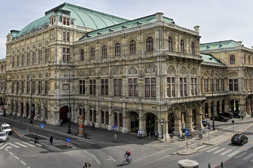 Ein großes, historisches Gebäude mit aufwendiger Architektur, einem begrünten Dach und einer belebten Straße davor. 5