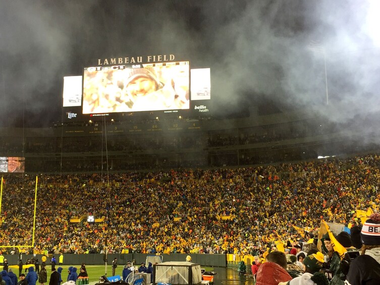 A stadium filled with spectators, a large digital scoreboard, and smoke in the air. 5