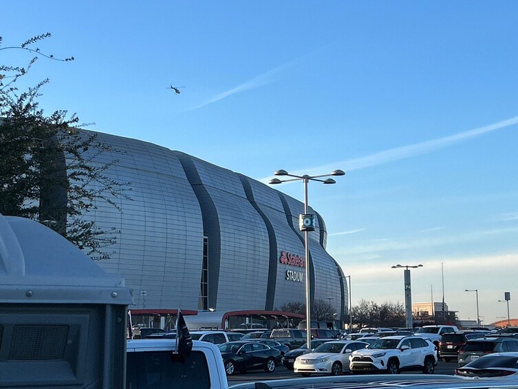 Un stade sous un ciel dégagé, avec des voitures garées et un hélicoptère en vol. 4