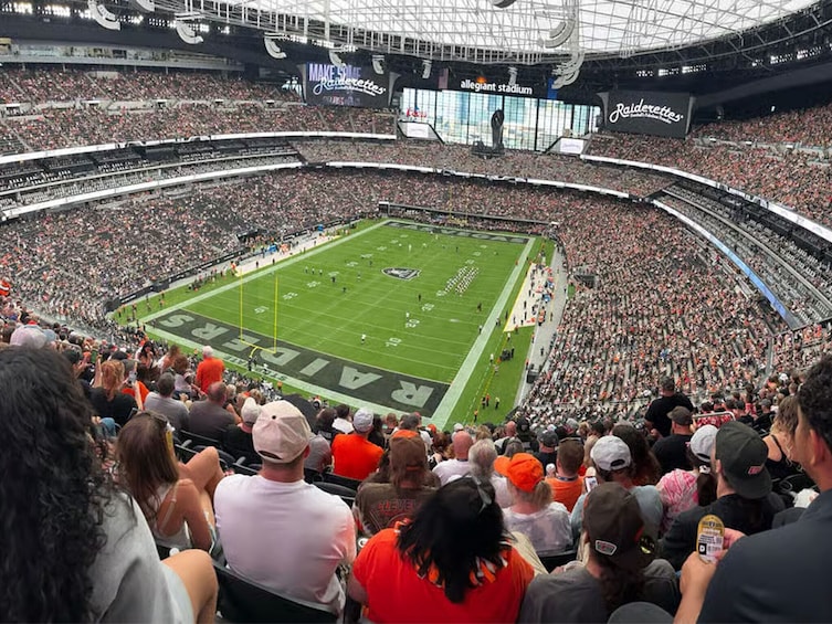 Uno stadio di calcio gremito di spettatori, un campo da gioco e pubblicità delle Raiderettes e di altri marchi. 1