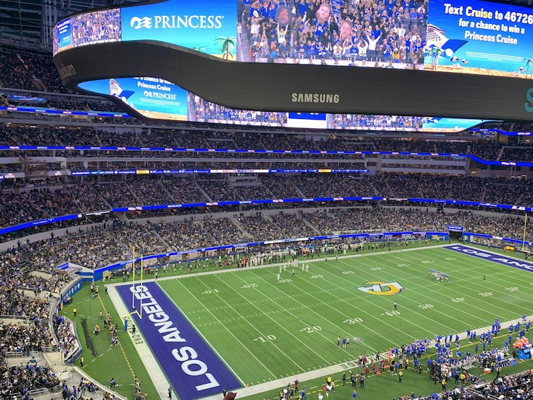Un stade de football doté d’un grand écran publicitaire pour une croisière, un terrain marqué des logos des équipes et une foule de spectateurs. 5