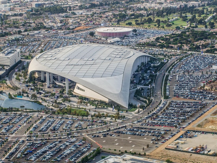 Un stade moderne doté d’un toit incurvé original, entouré d’un vaste parking et de bâtiments urbains. 4