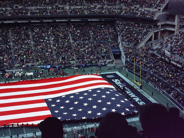 Una gran bandera estadounidense en un campo de fútbol con espectadores en un estadio. 5