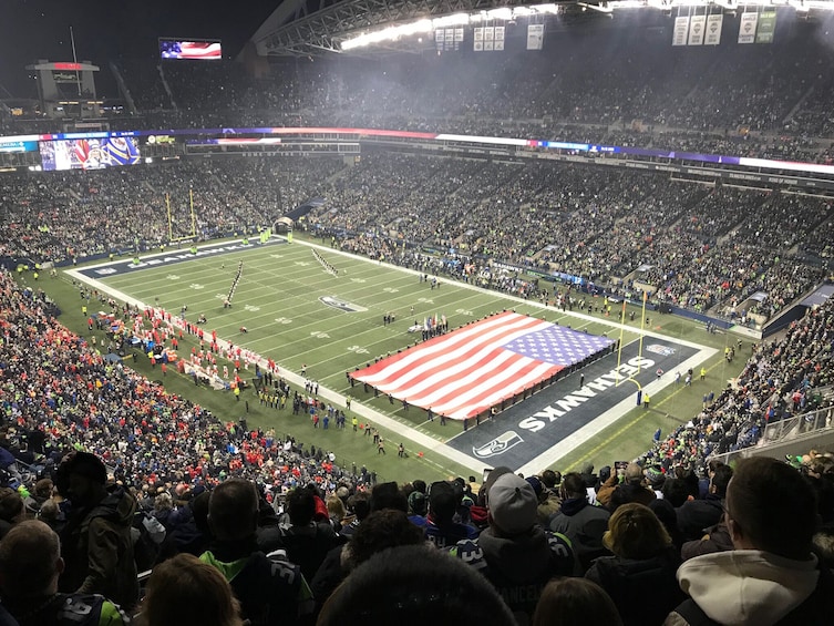 Un estadio de fútbol con una gran bandera estadounidense en el campo, rodeado de espectadores. 1