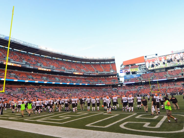 A football stadium with empty stands, a football field, and players lined up on the field. 5