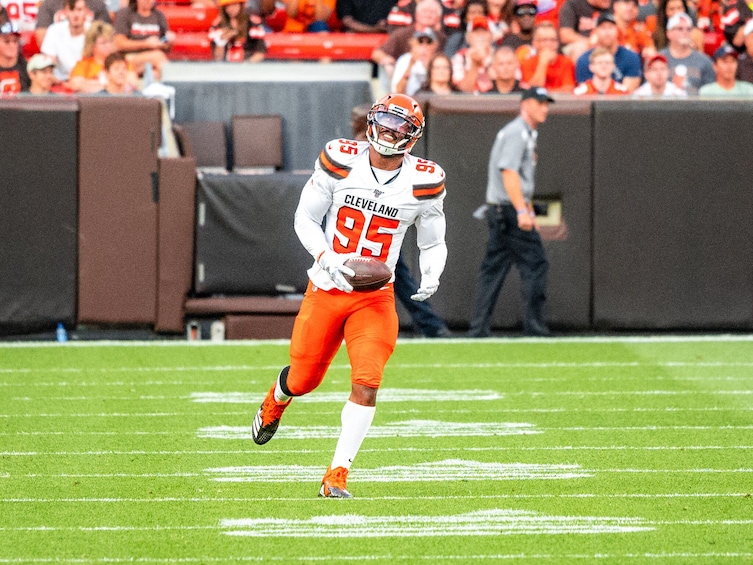 A football player in a white and orange uniform with the number 95, running on a field. 3