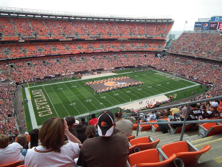 A football stadium with a large crowd, a marching band on the field, and the word 'CLEVELAND' on the sidelines. 4