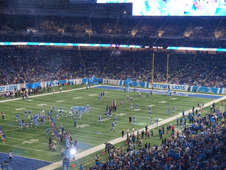 Et fodboldstadion fyldt med et stort publikum, en fodboldbane og reklamer for Detroit Lions. 1