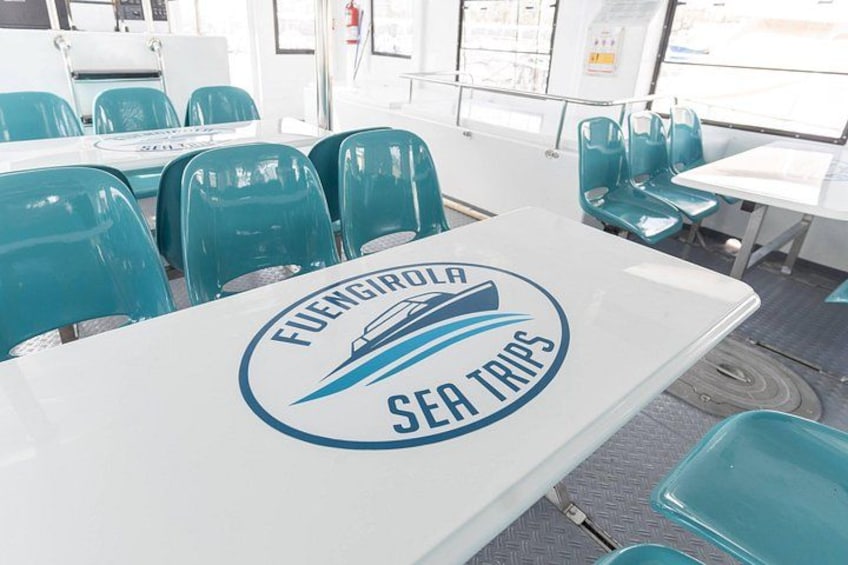 Un tavolo con il logo di 'Fuengirola Sea Trips' e diversi sedili verdi intorno. 2