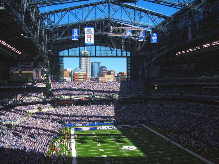 A football stadium filled with spectators, a large scoreboard, and a city skyline in the background. 5