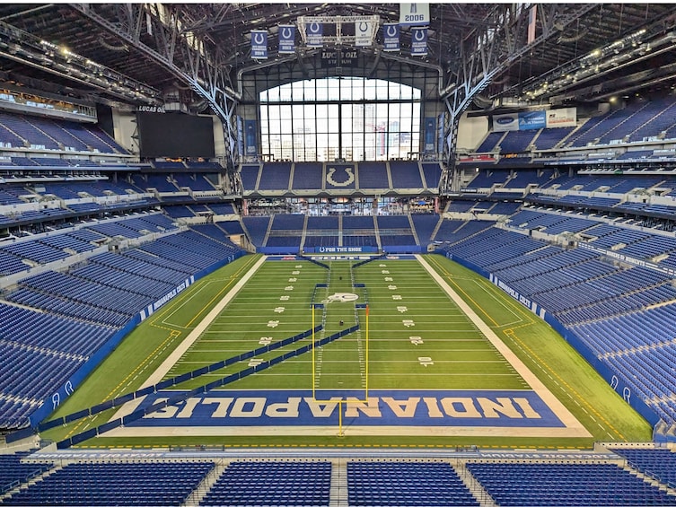 An empty stadium with blue seats, a football field, and the word 'INDIANA' on the end zone. 4