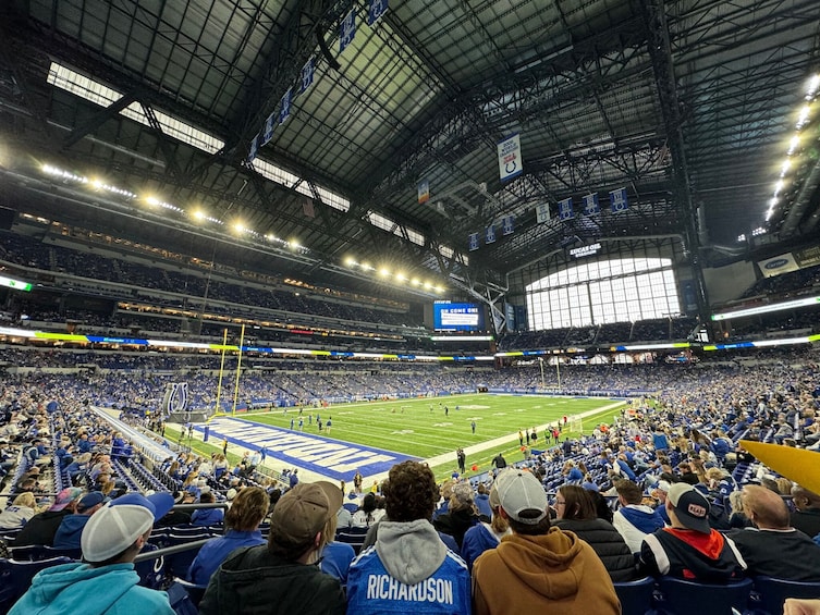 A large indoor stadium with multiple levels of seating, a football field, and a scoreboard. 1