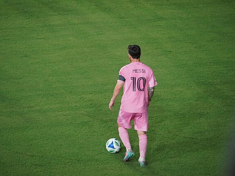 A soccer player in a pink jersey with the number 10 and the name 'MESSI' on the back, standing on a green field with a soccer ball at his feet. 3