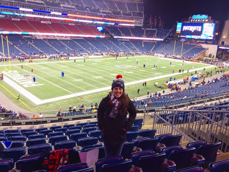 A football stadium with a large screen displaying a game, a person standing in the foreground, and empty blue seats. 1
