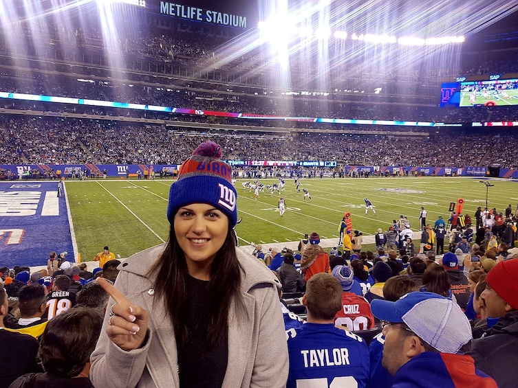 A person in a stadium with a large crowd, a football field, and the MetLife Stadium sign. 1
