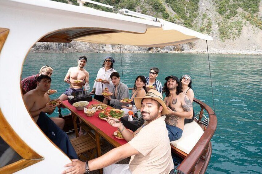 Un groupe de personnes est réuni autour d’un repas sur un bateau, avec une côte rocheuse en arrière-plan. 5