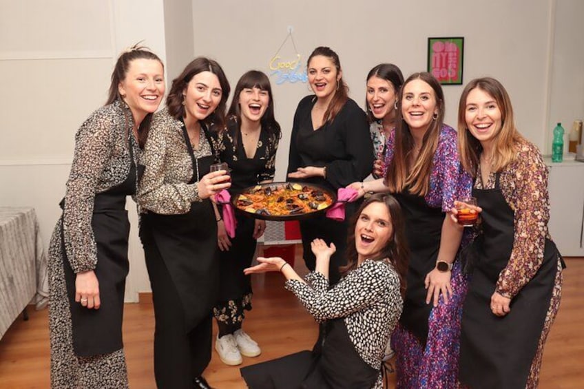 Un gruppo di persone che posa con una pizza grande in una stanza con pavimento in legno e pareti bianche. 3