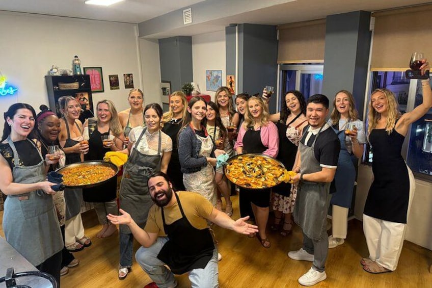 Un gruppo di persone tiene in mano una pizza in una stanza con pavimento in legno e un neon sullo sfondo. 5