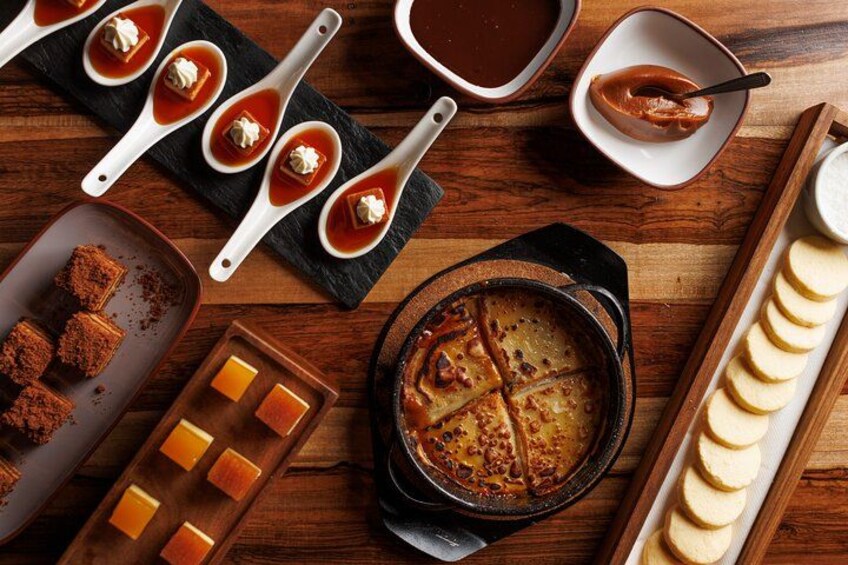 A wooden table with various food items, including a pot of soup, a plate of bread, and several bowls of sauce. 3