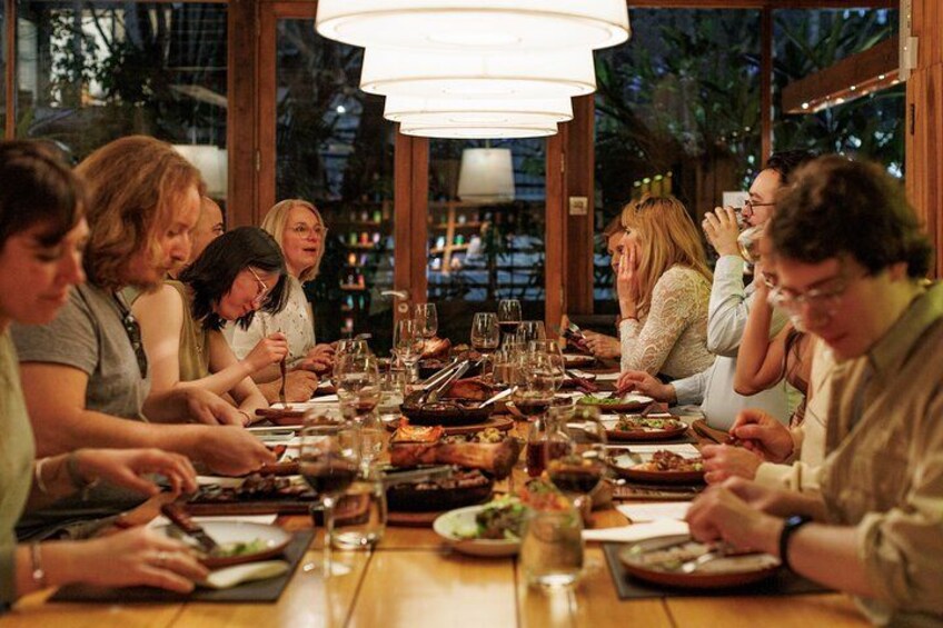 A group of people dining at a wooden table with a chandelier above. 1