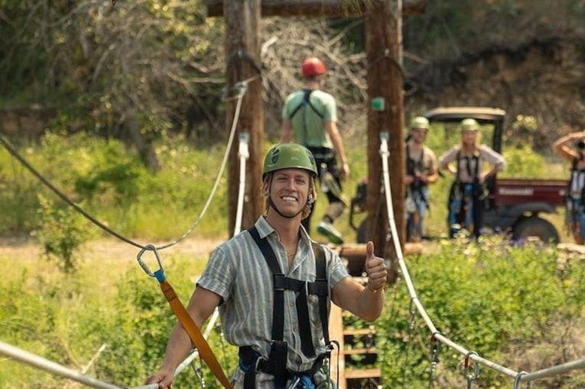 A person in a harness and safety gear, giving a thumbs-up, with a rope and pulley system in the background. 3