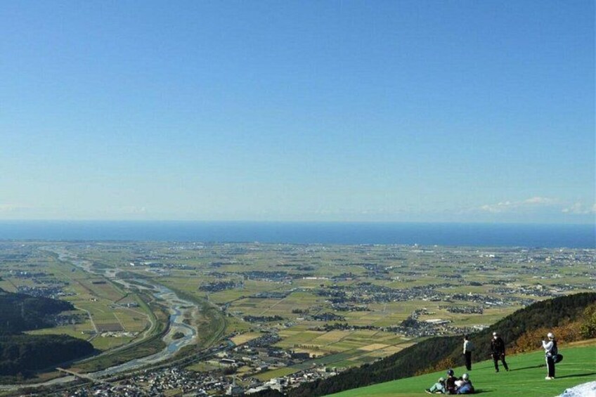 A panoramic view of a coastal landscape with a river, green fields, and a few buildings. 1