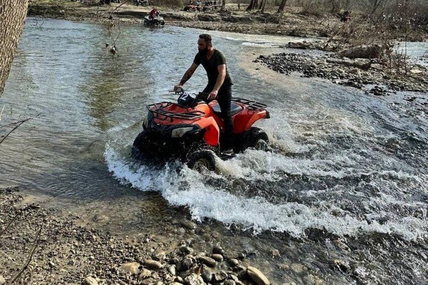 A person riding an ATV through a shallow river. 1