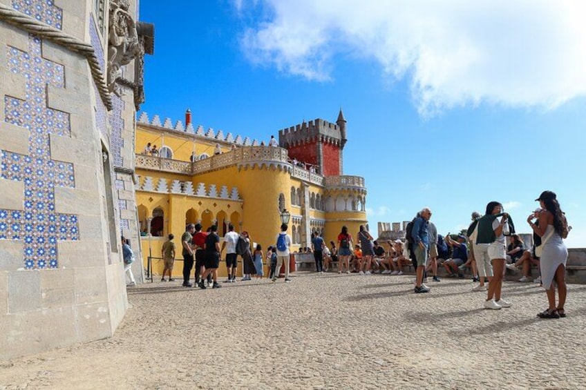 A historic building with tiled walls and a red-tiled roof, surrounded by a cobblestone courtyard with people. 3