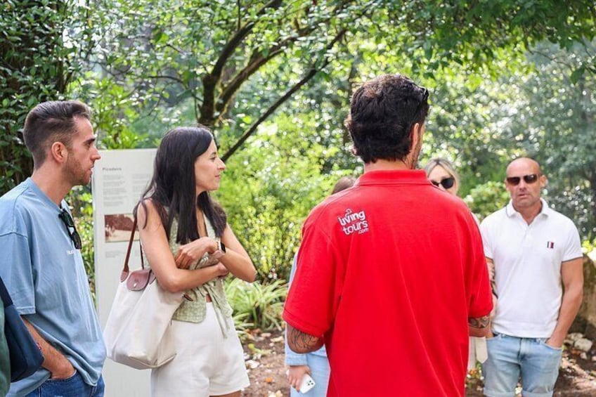A group of people standing outdoors, some wearing branded shirts, with greenery and trees in the background. 4