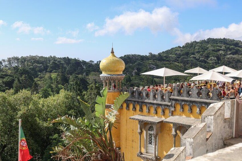 A historic building with a golden dome, a flag, and lush greenery in the background. 2
