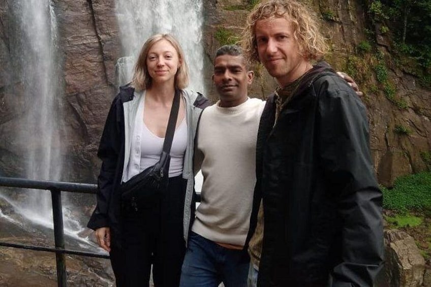Three people standing in front of a waterfall with a rocky background. 4