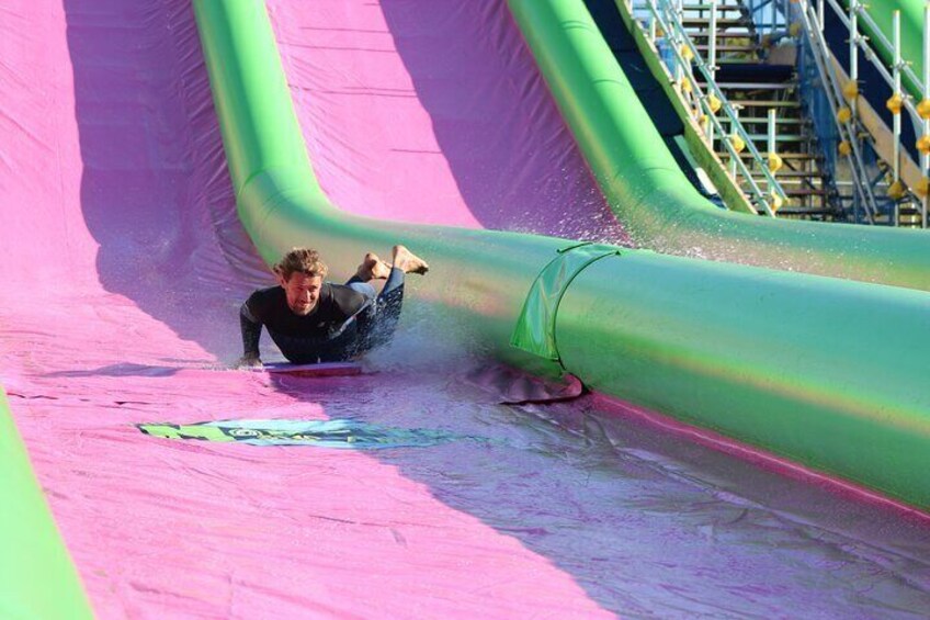 Une personne dévale une toboggan aquatique sur fond rose et vert. 2